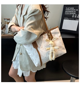 Detail of cream tote bag with butterfly prints and a plush rabbit charm accessory