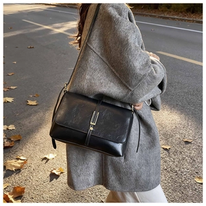 Detail of a black vintage crossbody bag with gold buckle on a model in an autumn street setting