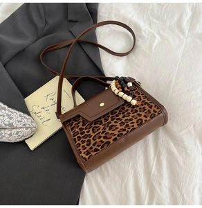Detail of leopard print crossbody bag with brown leather accents and beaded charm accessory