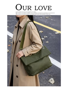 Detail view of a large olive green messenger bag with wide strap on a khaki trench coat
