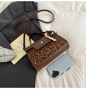 Close-up of leopard print crossbody bag with beaded charm on white bedding