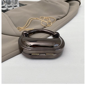 Detail of a gunmetal metallic evening clutch with a semi-circular handle on a beige blazer