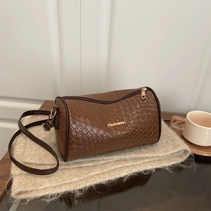 Brown woven cylinder shoulder bag with gold logo on a cozy knit background