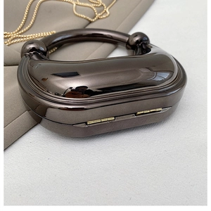 Macro view of gunmetal mirror finish evening bag with circular metal handle and gold chain