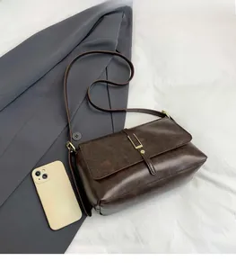 Dettaglio della borsa a tracolla vintage marrone scuro con patta e fibbia in metallo su abito