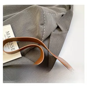 Dettaglio del manico in pelle marrone e del blazer grigio con fini cuciture bianche
