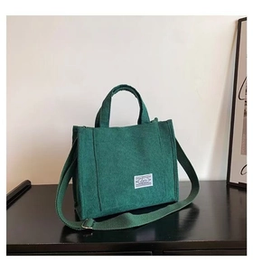 Detail of dark green corduroy tote bag featuring vertical texture and logo patch