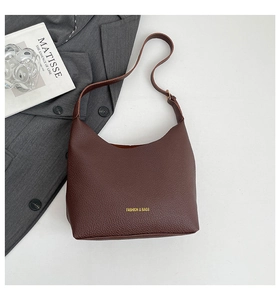 Macro detail of brown lychee grain leather tote bag with gold logo and shoulder strap