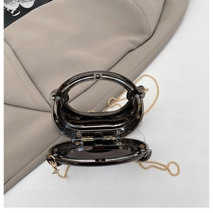 Detail of round acrylic clutch bag showing the open magnetic clasp and golden chain