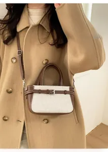 Détail d'un sac bandoulière en cuir marron et toile beige porté sur un manteau