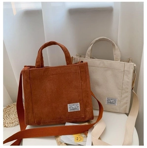 Detail of corduroy tote bags in rust and beige with woven label and wide shoulder straps