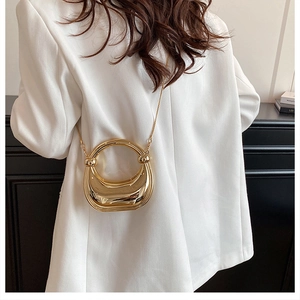 Detail of a shiny gold metallic mini crossbody bag with a sleek semi-circle handle