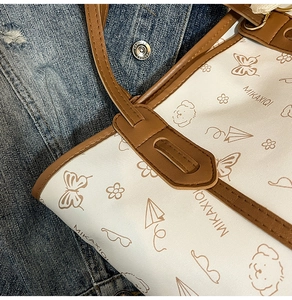 Detailed close-up of white tote bag with cartoon patterns and premium brown leather straps