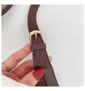 Close-up of brown pebbled leather shoulder strap with adjustable light gold metal buckle