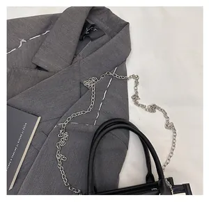 Detail of a chic black crossbody bag with a slim silver chain strap on a grey blazer