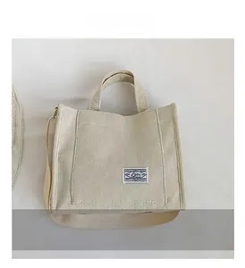 Detailed close-up of cream corduroy tote bag featuring front pocket and woven label