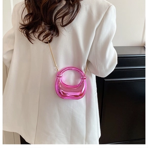 Detail of a bright pink mirror metallic mini crescent bag with a gold chain strap