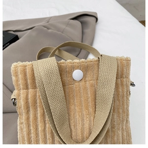 Detail of light camel corduroy mini tote bag texture and top button closure on a blazer
