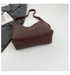 Detail of dark brown litchi grain leather texture and gold logo on the trendy tote bag