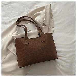 Vue de dessus d'un sac cabas léopard marron sur tissu blanc avec accessoires minimalistes