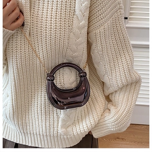 Detail of a shiny dark brown mini half-moon bag with gold chain strap on a white sweater