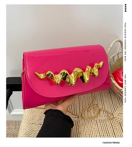 Close-up of rose red patent leather flap bag with wavy gold buckle and metal chain strap