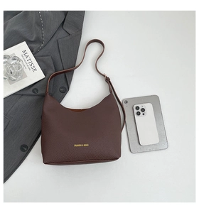 Flat lay of brown leather hobo bag next to a tablet and book on white background