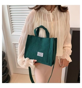 Close-up of dark green corduroy tote bag featuring a white decorative woven label