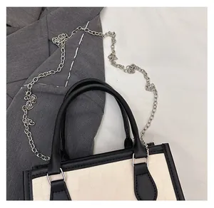 Detail of a chic tote bag featuring black leather handles and silver metal chain strap