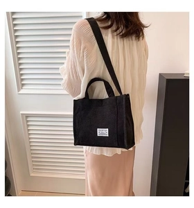 Detail of minimalist black canvas tote bag with wide strap worn as a crossbody bag