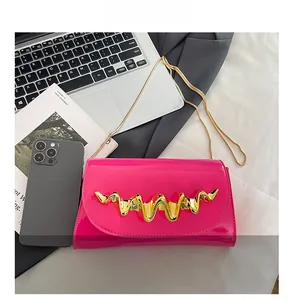 Detail of fuchsia patent leather mini bag with gold chain and wavy metal clasp on a desk