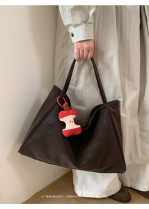 Dettaglio della borsa tote marrone scuro con ciondolo a mela e stile retrò minimalista