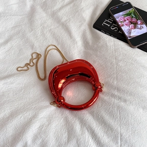 Glossy red circular handbag with gold chain strap on white fabric background