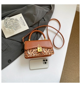 Close-up of leopard print patchwork leather bag with golden twist lock on white desk