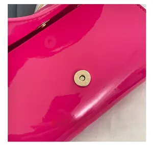 Detail view of the metallic magnetic closure on a magenta glossy patent leather handbag