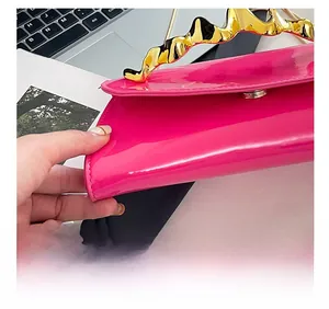 Detail of fuchsia patent leather handbag featuring unique wavy gold metal handle and stitching