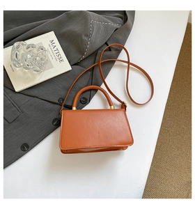 Flat lay of caramel leather crossbody bag with top handle next to a magazine