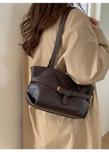 Dettaglio di una borsa sottobraccio in pelle marrone scuro con fibbia su un trench