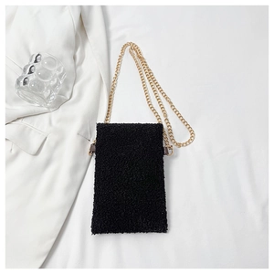 Detail of black teddy fleece mini bag with gold chain strap on white fabric background