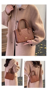 Detail of a brown embossed crossbody bag with gold chain and top handles on model
