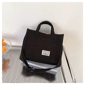 Versatile black corduroy tote bag with adjustable shoulder strap and handle on stand