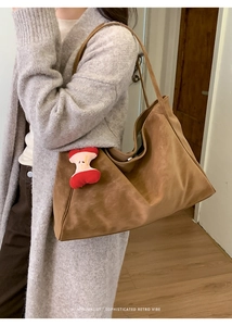 Borsa tote in pelle scamosciata marrone con charm a mela rossa indossata su cardigan
