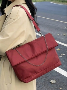 Detail of red nylon tote bag with metal chain strap worn by a woman in beige trench coat