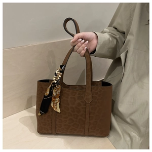 Détail du sac cabas en daim marron à motif léopard avec un foulard en soie sur l'anse
