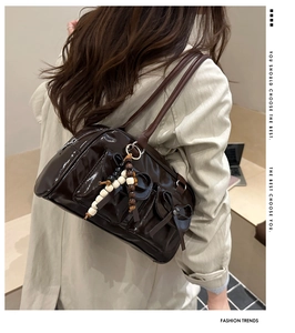 Rear view of a dark brown glossy shoulder bag with bow detail and beaded keychain