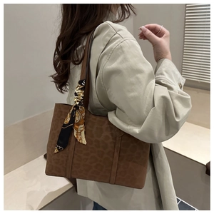 Detail view of large brown leopard print tote bag with decorative silk scarf accessory