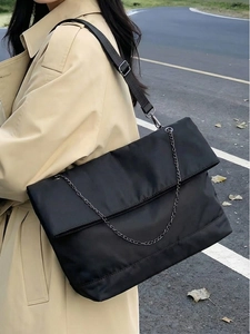 Close-up of black nylon tote bag with metal chain detail on model in beige trench coat
