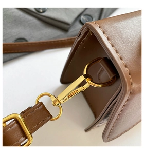 Detailed macro of golden metal clasp and stitching on the brown leather crossbody bag