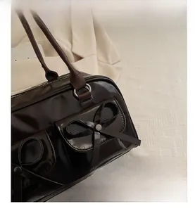 Detail of dark brown glossy leather handbag featuring side bow knot and metallic button