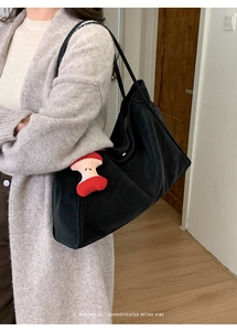 Dettaglio di una grande borsa tote nera con un originale ciondolo a forma di torsolo di mela